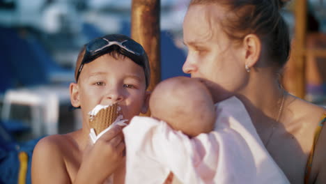 madre con el bebé y el hijo mayor en la playa niño comiendo helado