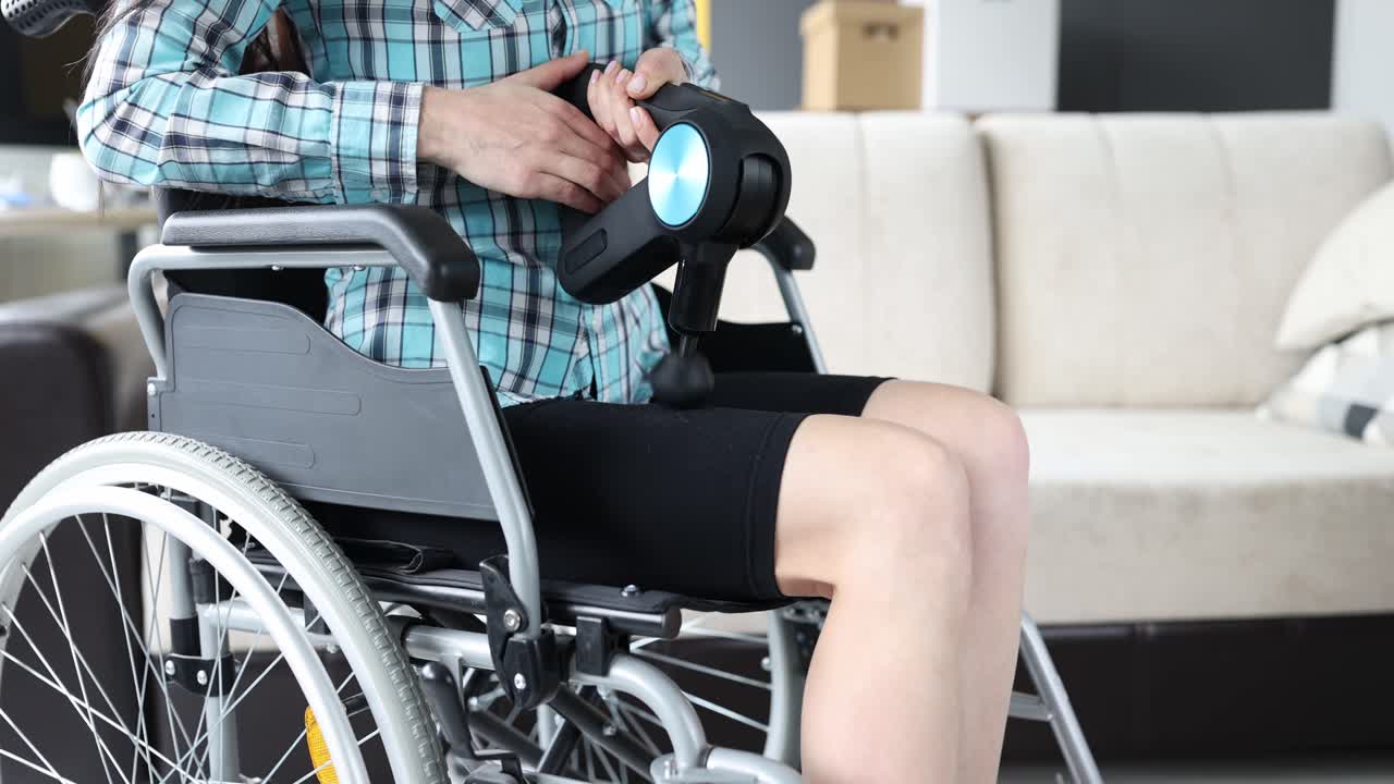 Woman in a wheelchair massaging her leg with percussion massager 4k movie