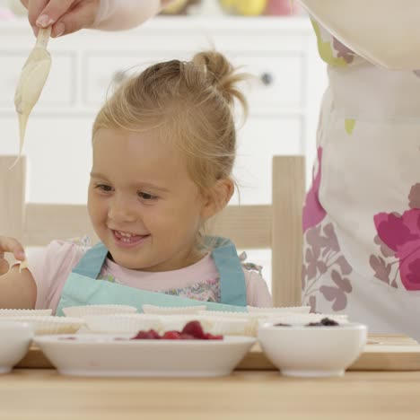 niña riendo con tazas de muffin y padre en delantal