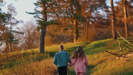 young couple having a scamper in the morning. guy and a girl holding hands and running together up the hill in the forest. rear view.