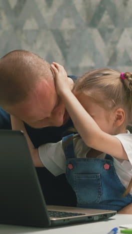 slow motion: cute little girl shakes father head having fun near modern laptop at white table in brightly lit apartment staying home at quarantine time