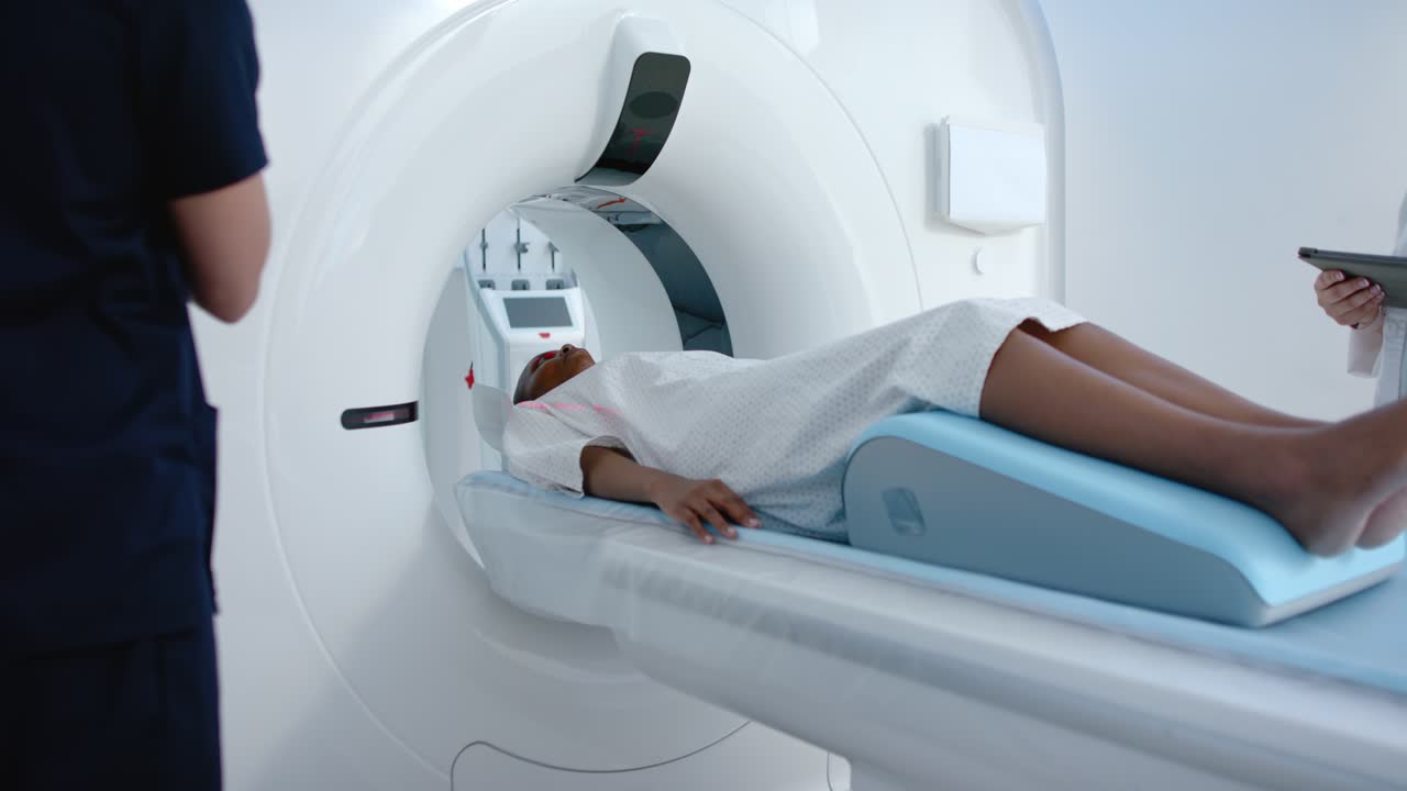 Paziente in camice disteso sul lettino, che scivola nello scanner mentre il tecnico utilizza il pannello per avviare la scansione