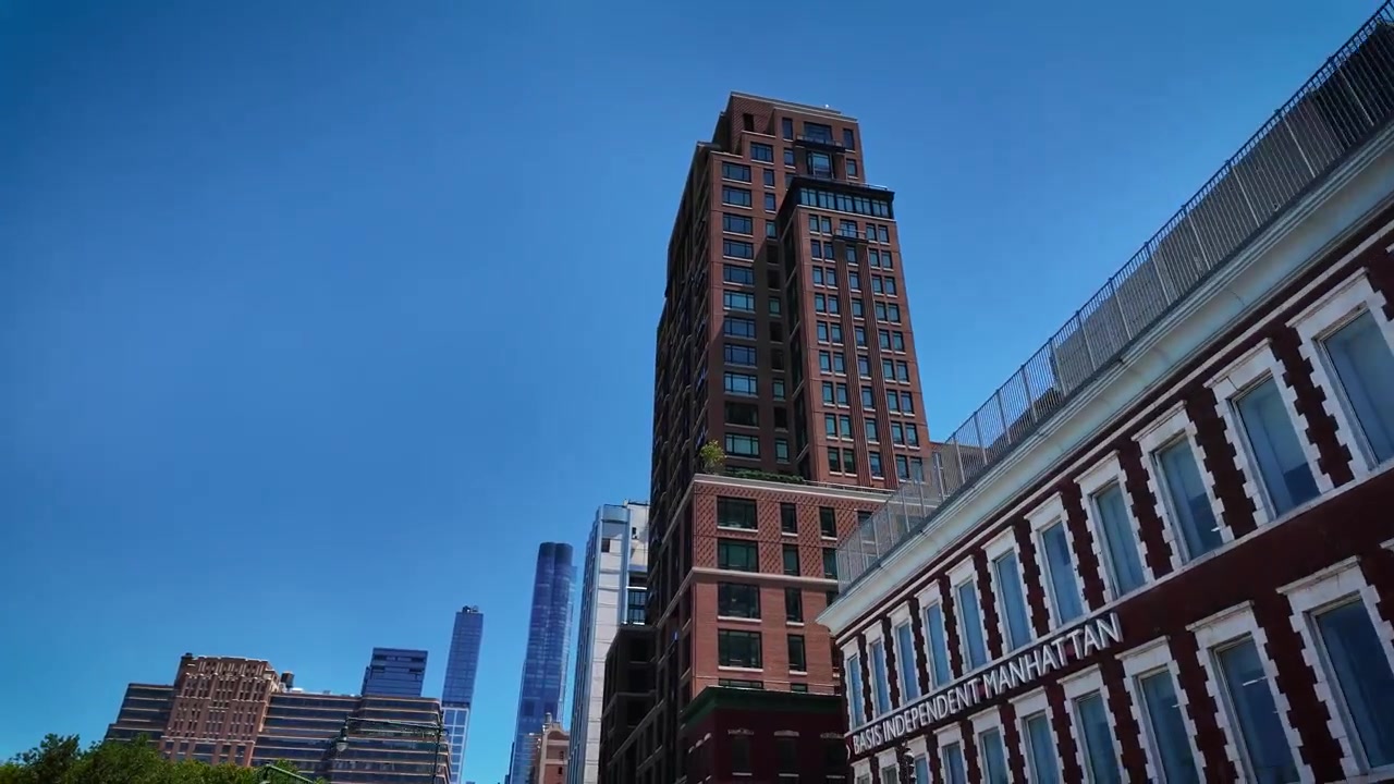 Toma desde un vehículo pasando edificios residenciales y comerciales modernos en Chelsea, Manhattan, mostrando arquitectura urbana contemporánea en un día de verano soleado y brillante