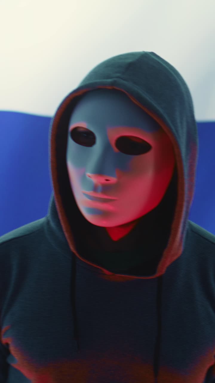 Maskeret hacker i hættetrøje stående foran russisk flag