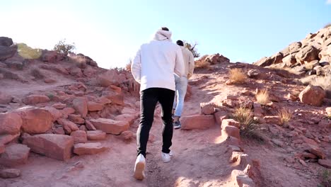 two guys hiking up red rock stairs in the desert