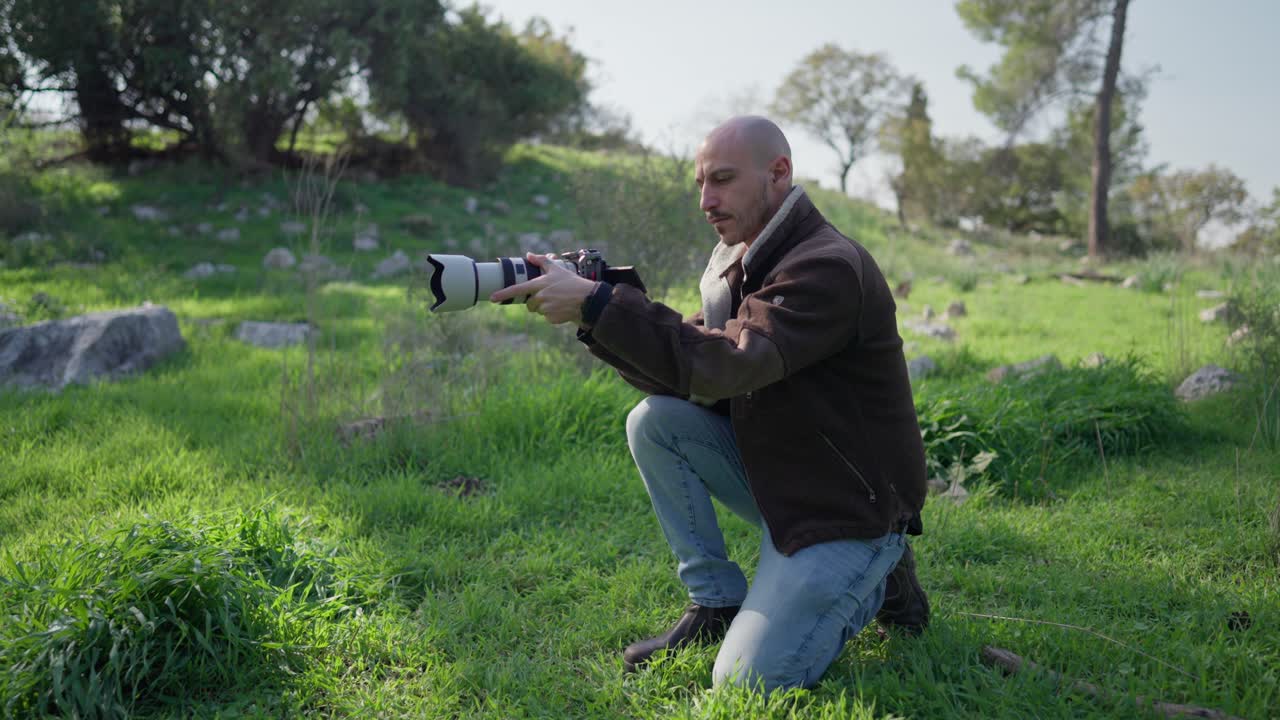 Camera operator kneeling in a green forest while filming a low angle shot with a professional mirrorless camera