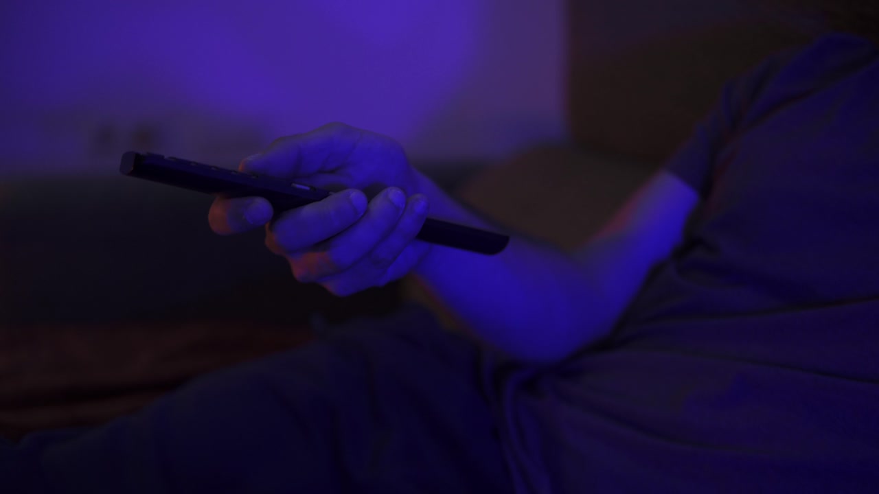 primer plano de un hombre presionando botones en un control remoto de televisión con la habitación parpadeando con luz