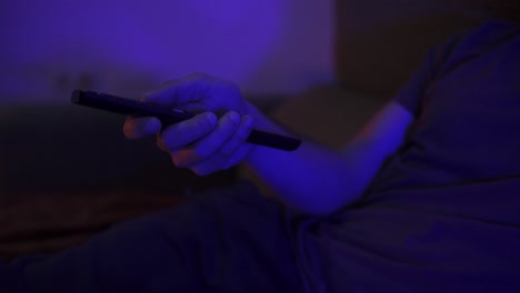 primer plano de un hombre presionando botones en un control remoto de televisión con la habitación parpadeando con luz