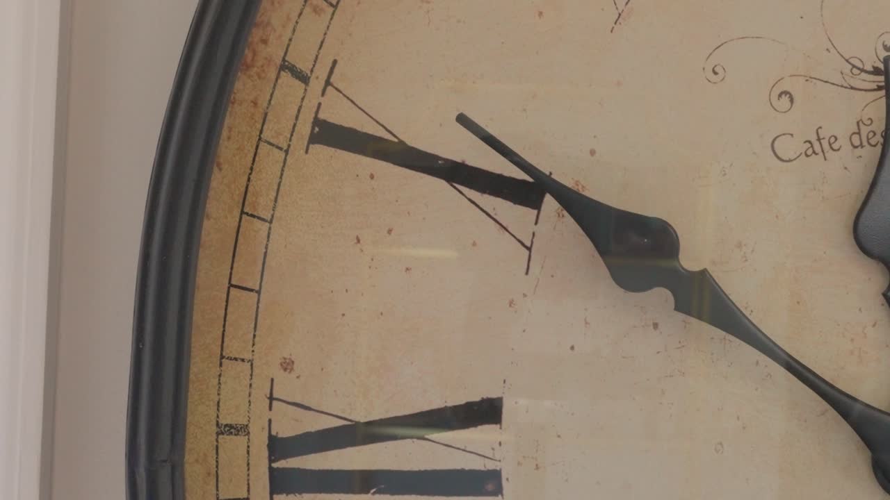 Close up of minute hand on a clock ticking across Roman numeral 10. The image rotates slight and zooms in.
