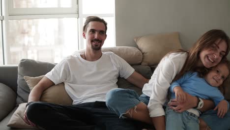 Portrait-of-happy-caucasian-family-sitting-embraced-on-sofa-in-living-room-in-slow-motion.-Mother-bonding-their-little-naughty