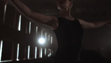 prima ballet company in a dark dress on a dark theater stage rehearsing in the smoke performs dance moves in slow motion.