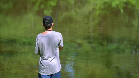 Back-of-teenage-boy-casting-a-fishing-rod-into-calm-water-on-a-sunny-afternoon