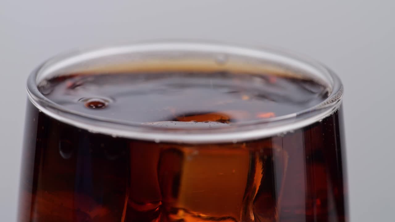 cerca de cubos de hielo cayendo en un vaso de cola fresca sobre un fondo blanco