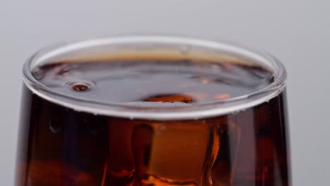 cerca de cubos de hielo cayendo en un vaso de cola fresca sobre un fondo blanco