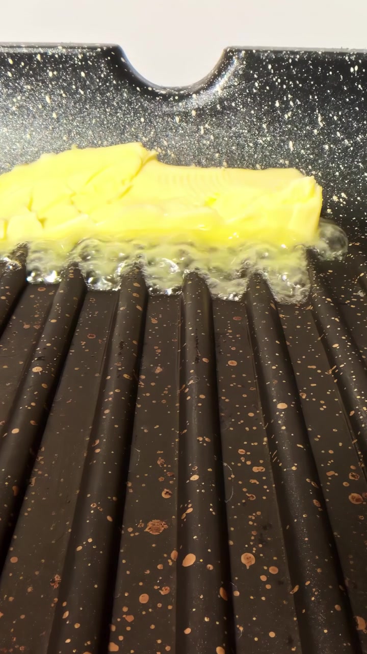 Vertical close-up of a block of butter foaming as it melts on a hot ridged grill pan
