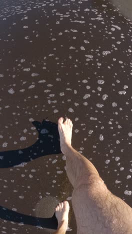 pov man's feet walking on a beach in spume of the waves, portrait