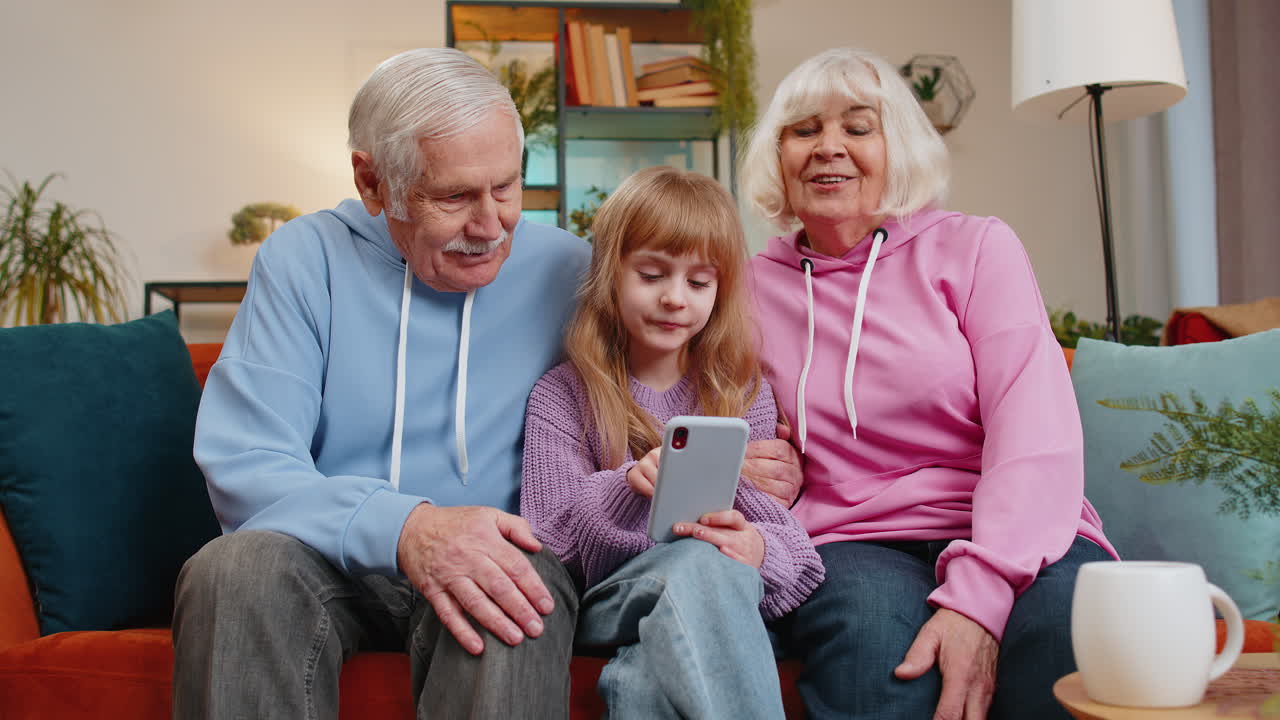 Ragazza nipote bambino che insegna a nonno e nonna usando lo smartphone sul divano nella stanza di casa