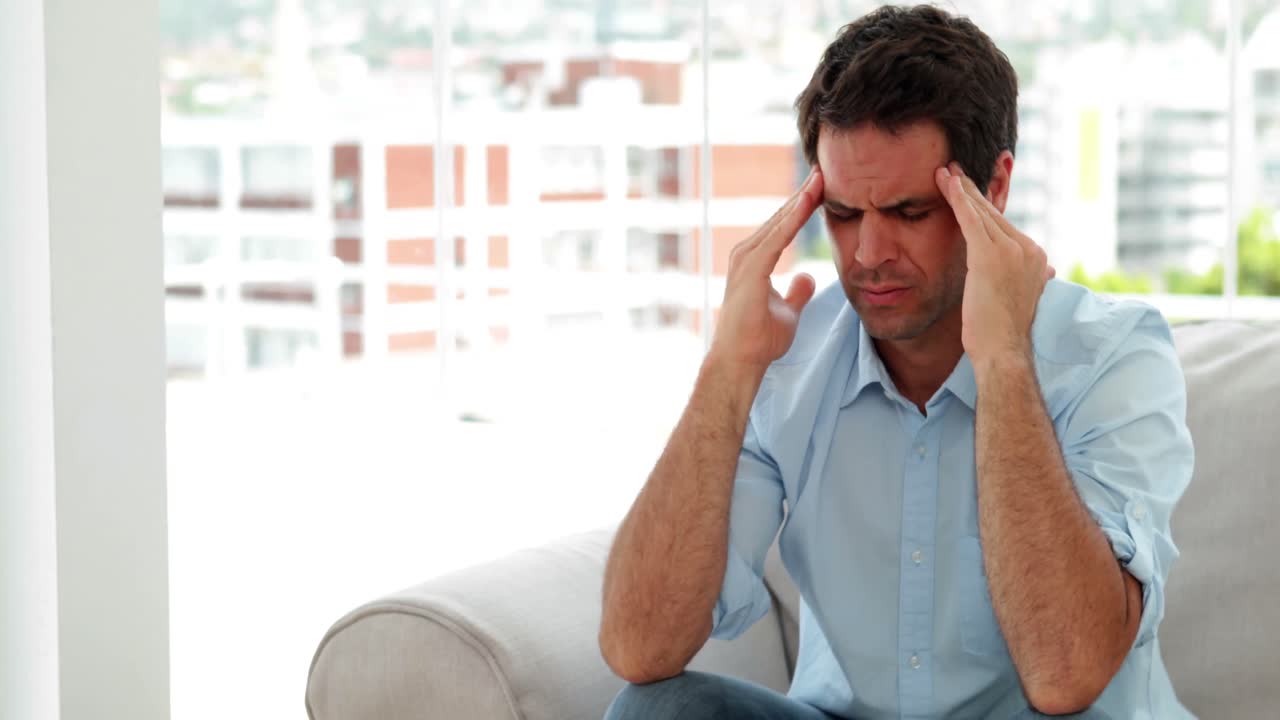 Casual man sitting on the sofa getting a headache