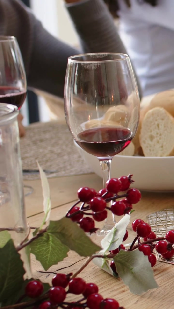 Video verticale: Angolazione in movimento che porta il vino sul tavolo di casa, con una persona in bianco che si allunga e una in grigio che gesticola.
