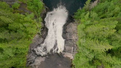 aerial rising shot above big waterfall and tall spruce trees