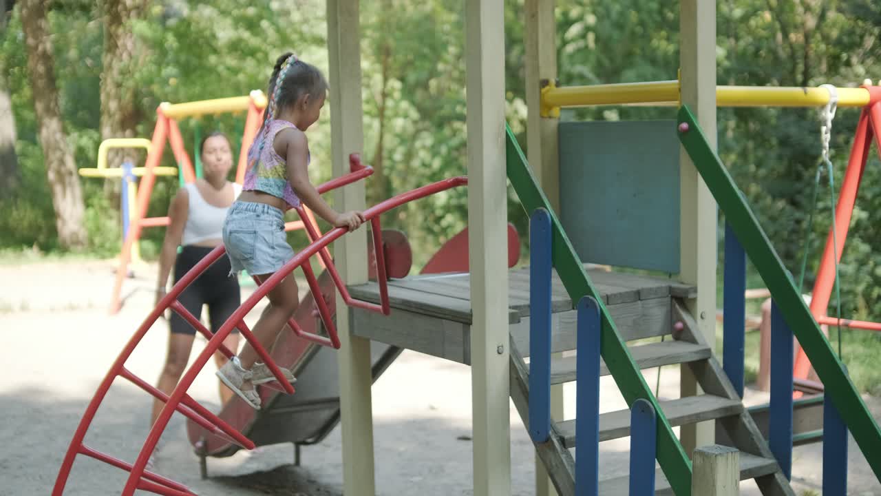 madre embarazada viendo a su hija jugar en el tobogán en el patio de recreo