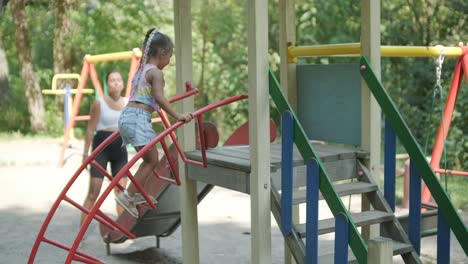 madre embarazada viendo a su hija jugar en el tobogán en el patio de recreo