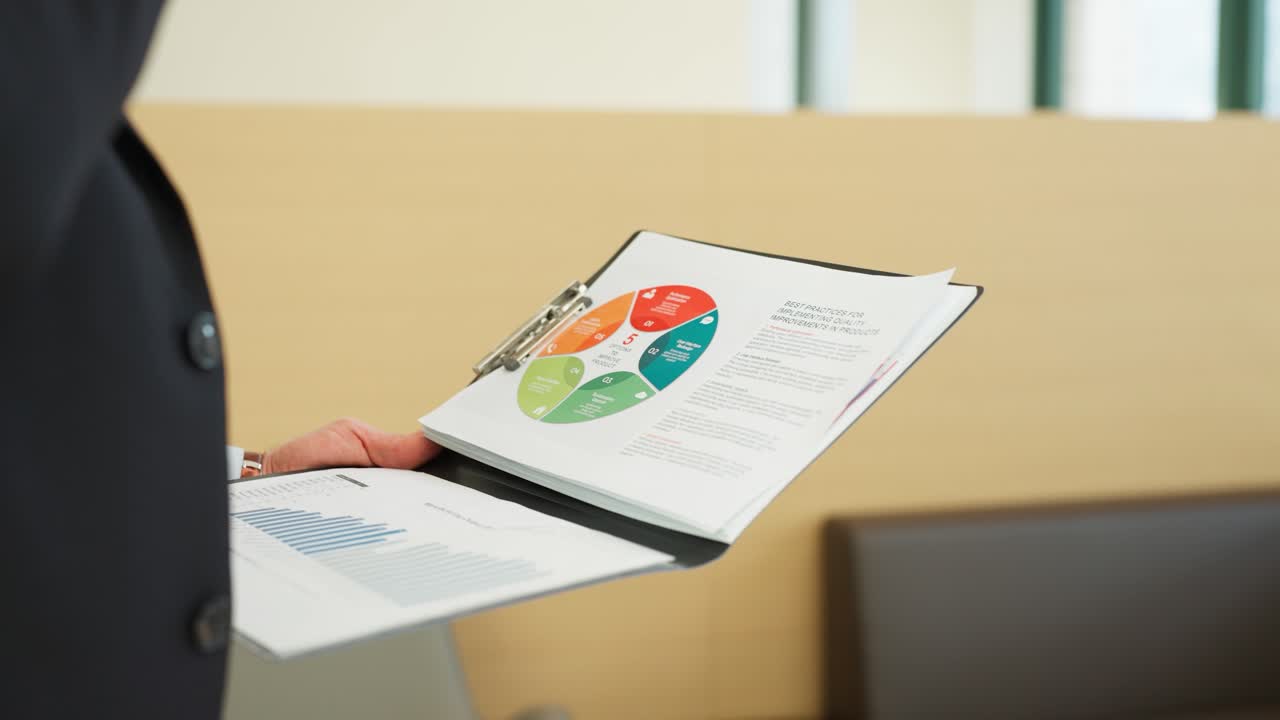 A person in formal attire holds a clipboard with documents, including a colorful pie chart and a bar graph, in a professional setting - parallax shot