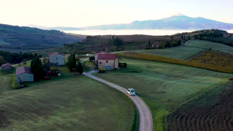 imágenes aéreas de drones de 4k de un automóvil, una camioneta que se mueve en una carretera vacía en los campos de otoño durante el amanecer en toscana, italia