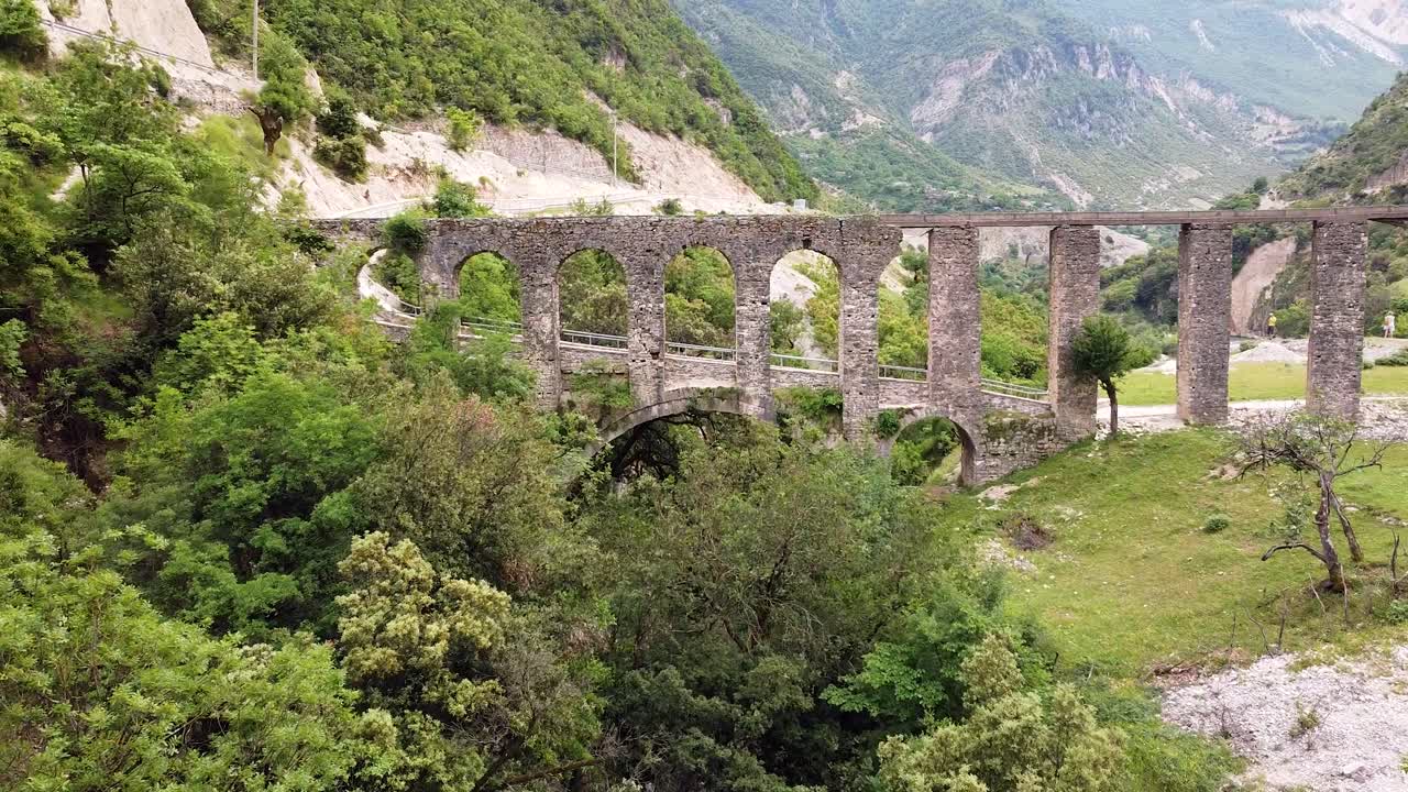 알바니아의 벤체에 있는 알리 파샤 수로 (ali pasha aqueduct) 의 드론 영상, 푸른 언덕과 산악 풍경으로 둘러싸인 역사적인 아치를 포착합니다.
