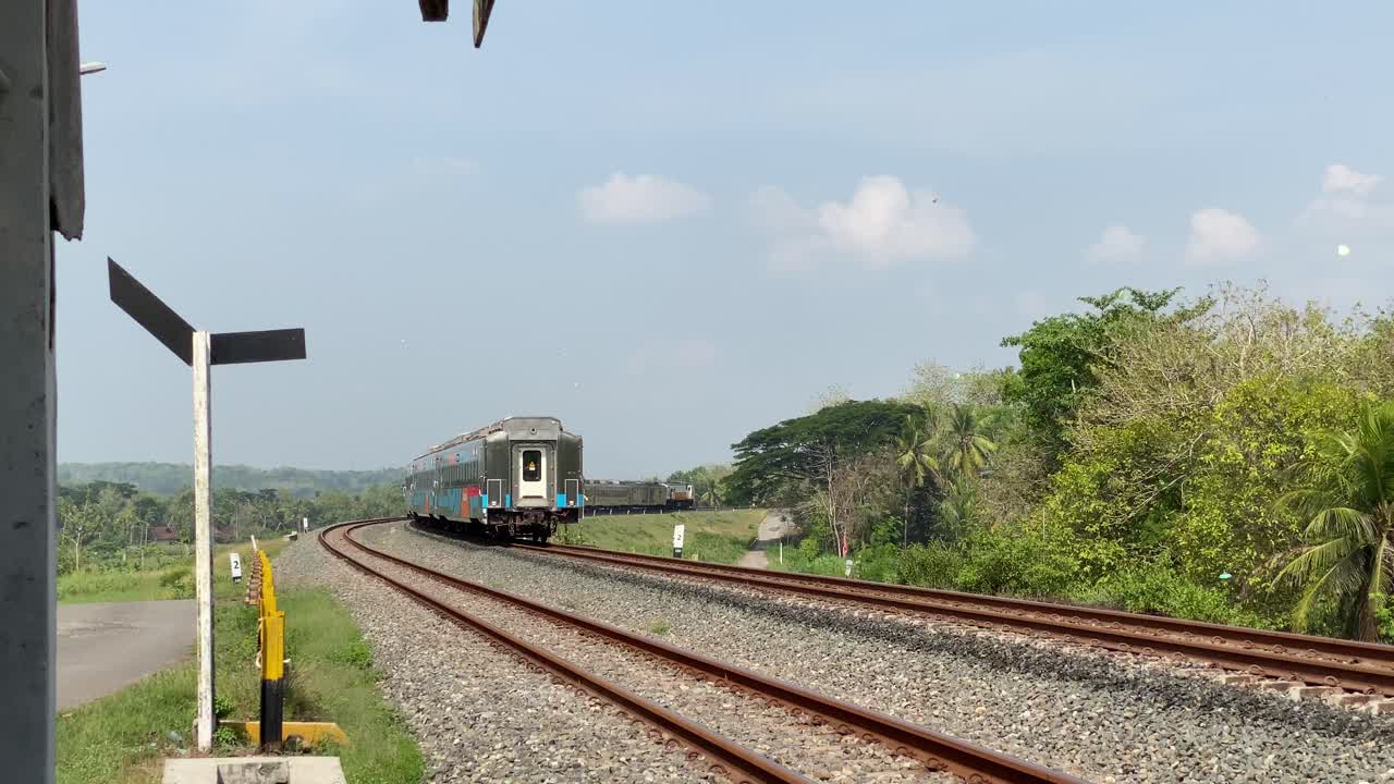 Passenger train passes through rural rice fields, curved double track