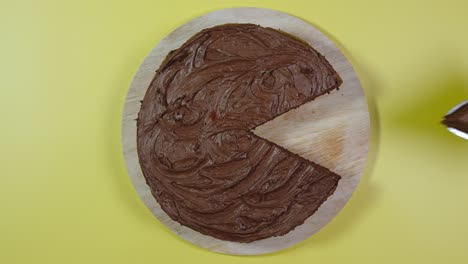 top view: man's hand picks up piece of chocolate cake on yellow surface