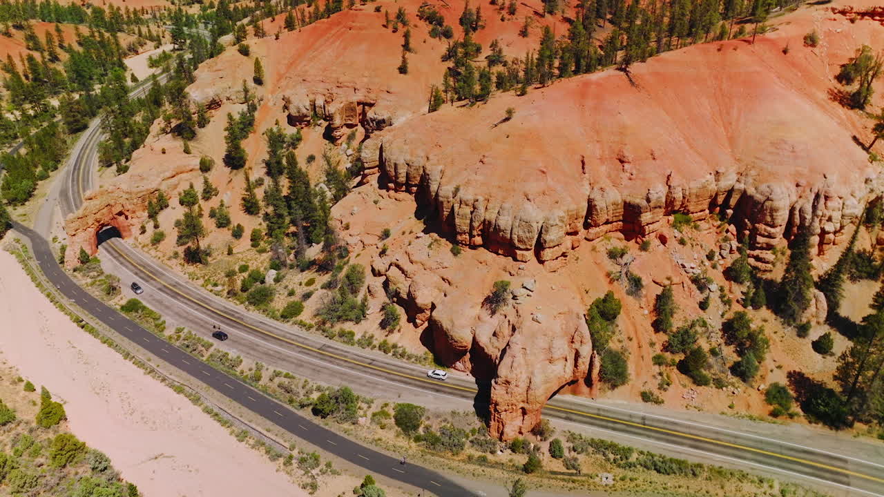 Sunlit panorama of amazing canyon rocks with pine trees growing on. Car roads in the mountains of Arches National park from aerial view.