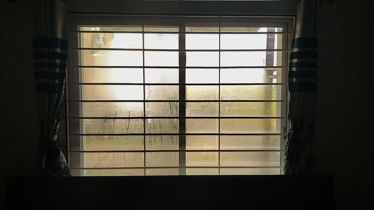 Camera in dark room slowly approaches window pane with fog water drops