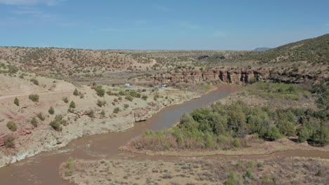 Aerial-view-of-car-pulling-into-hiking-trailhead-by-river-in-desert-landscape