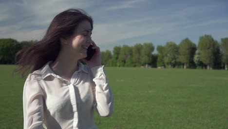 steadicam shot of a young beautiful italian girl in a great mood on while walking in the park and talking on the phone