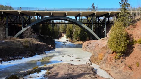 Vista-Aérea-Del-Río-Congelado-Bajo-El-Puente-De-Grosella-Espinosa-En-Minnesota