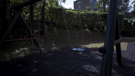 columpios vacíos en cámara lenta en el parque de juegos moderno rodeado de árboles verdes al atardecer