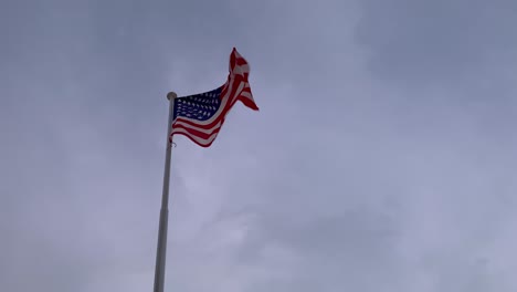 the flag of america flutters in the wind, with gray clouds in the background