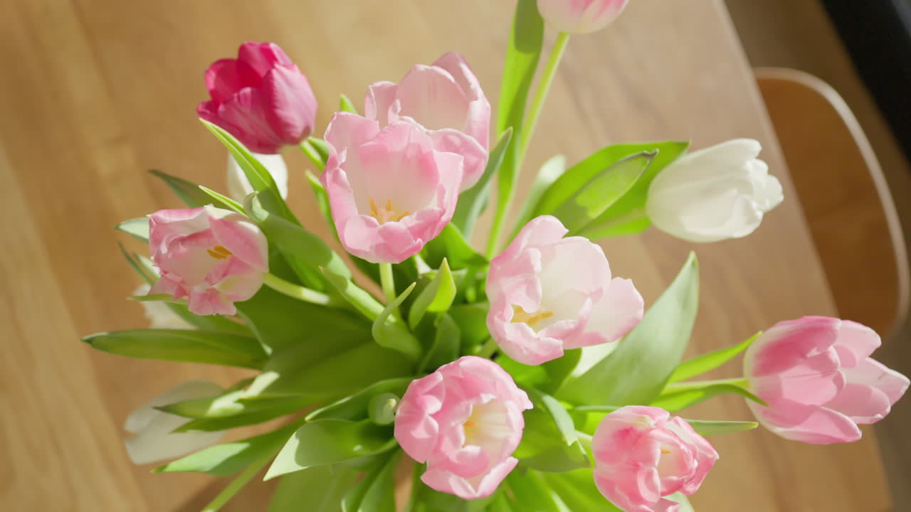 Top shot of delicate tulips in a vase, dollying out to reveal a warm, sunlit wooden table setting