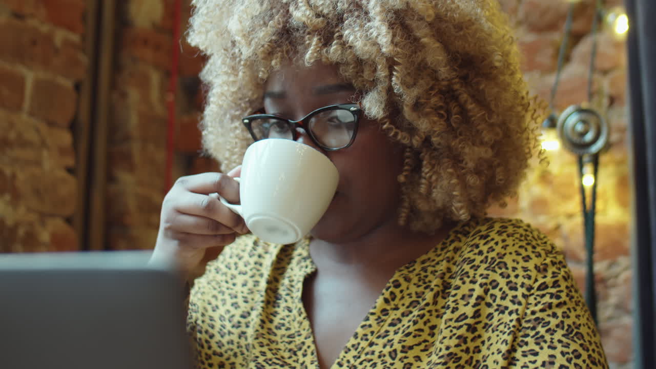 mujer afroamericana bebiendo café y usando una computadora portátil en un café