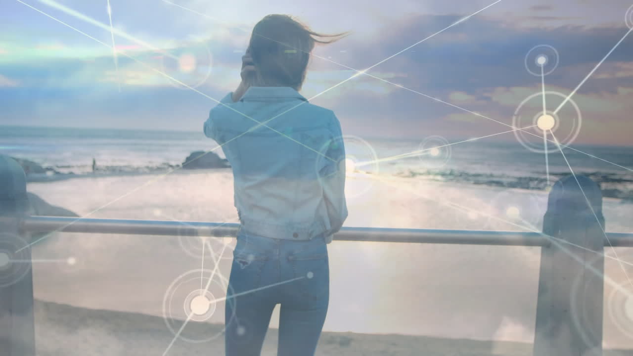Standing by ocean, woman with digital network animation overlaying scene