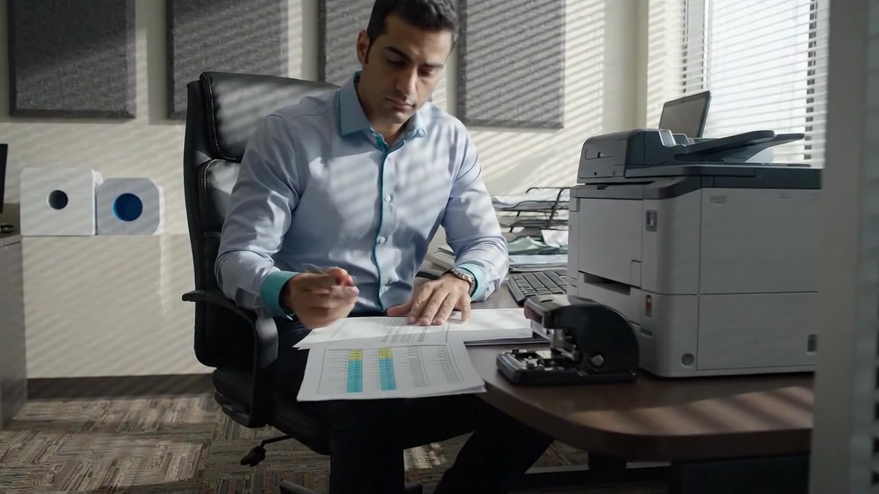 Un professionista concentrato impegnato nella revisione di documenti e nell'analisi in un ambiente d'ufficio moderno con una stampante di alta qualità e una postazione di lavoro.