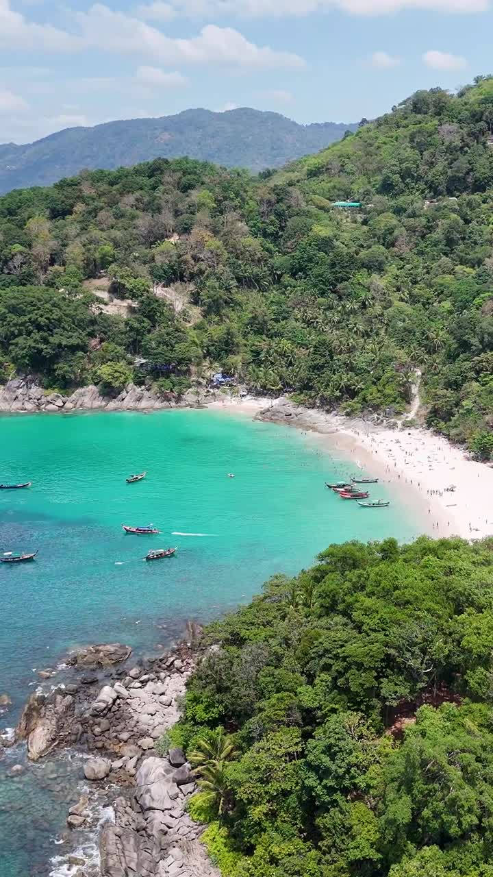 Un filmato di drone cattura una serena insenatura sulla spiaggia a Phuket, Thailandia, mostrando acque turchesi, vegetazione lussureggiante e un'atmosfera tranquilla.