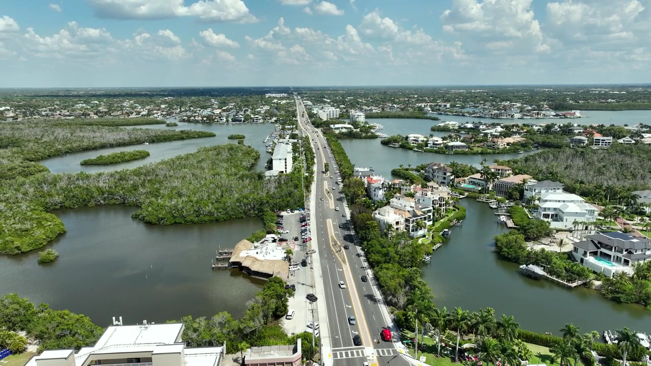 Prospettiva aerea dei rigogliosi estuari di mangrovie e delle case sul lungomare di Bonita Springs, con la costa del Golfo, condomini a più piani e zone umide tropicali che si estendono fino all'orizzonte.