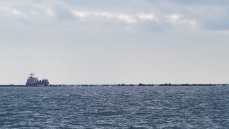 large red cargo ship leaves port of liepaja, calm bay in foreground, wide shot from a distance