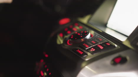 vista en primera persona de la mano de una mujer presionando el botón tel en un panel de control de coche por la noche. el tablero de instrumentos está iluminado con luces rojas, destacando los controles. disparado con una cámara de mano