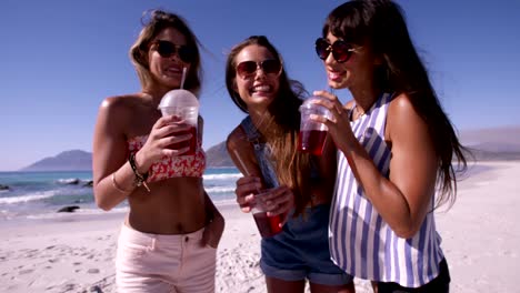 tres amigas jóvenes tomando bebidas en la playa
