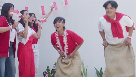 two asian young men participate in sack race called balap karung to celebrate indonesian independence day, august 17th.