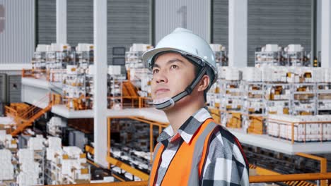 close up side view of asian male engineer with safety helmet standing in the warehouse with shelves full of delivery goods. looking around, checking the stock on racks