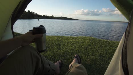 sunrise over serene lake from inside a camping tent while drinking coffee, caucasian male